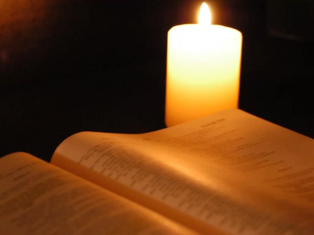 Una biblia abierta, con vela encendida en una habitación oscura propicia para una oración que mueva la misericordia de Dios